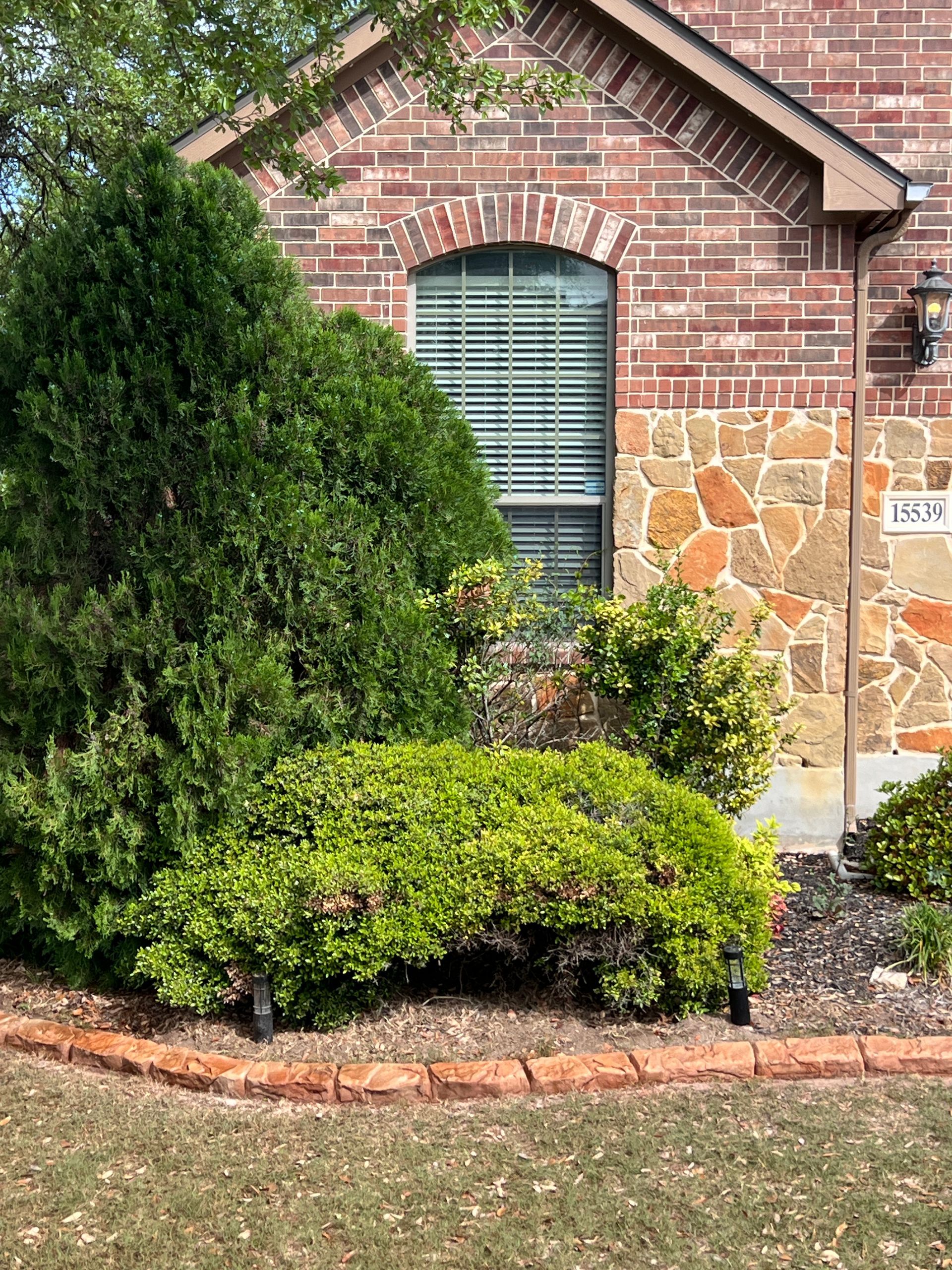 A brick house with a lush green garden in front of it.
