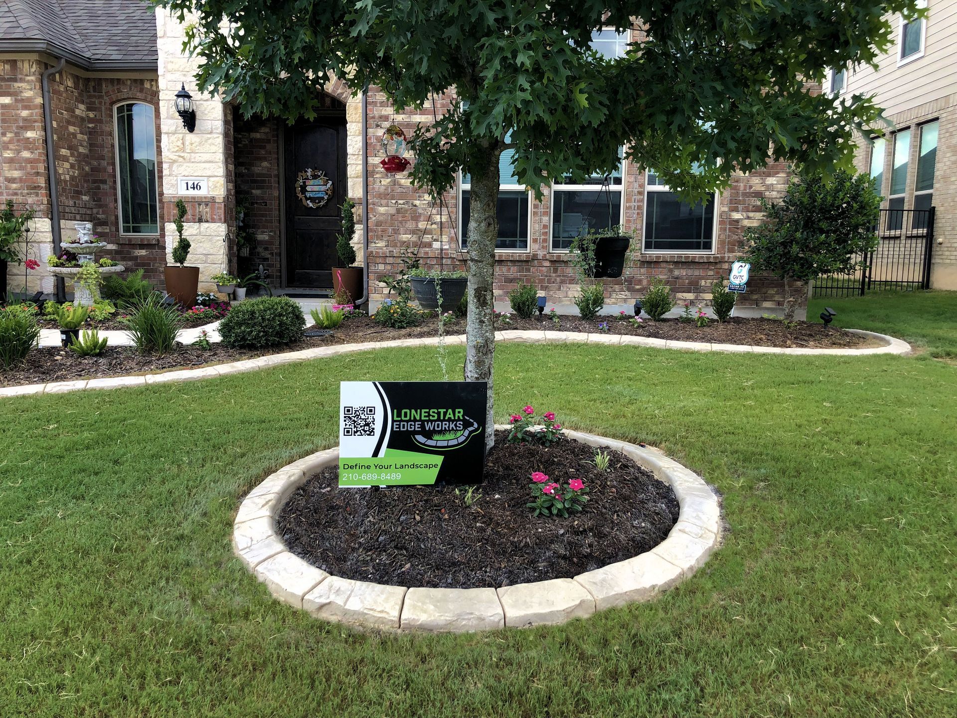 A tree in the middle of a lush green lawn in front of a house.