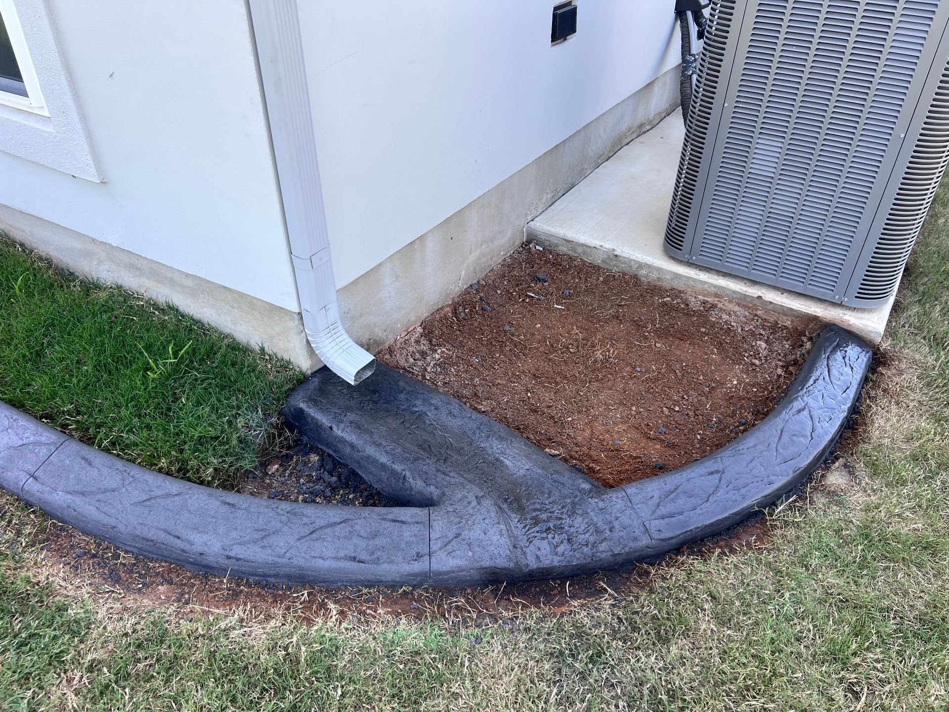 A concrete curb is sitting on the side of a house next to an air conditioner.