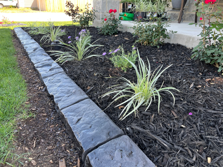 A garden with flowers and mulch and a stone border.