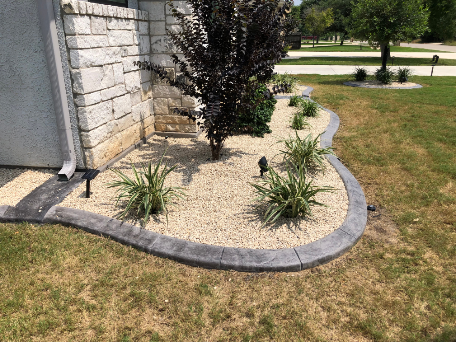 A garden with a concrete curb and gravel in front of a house.