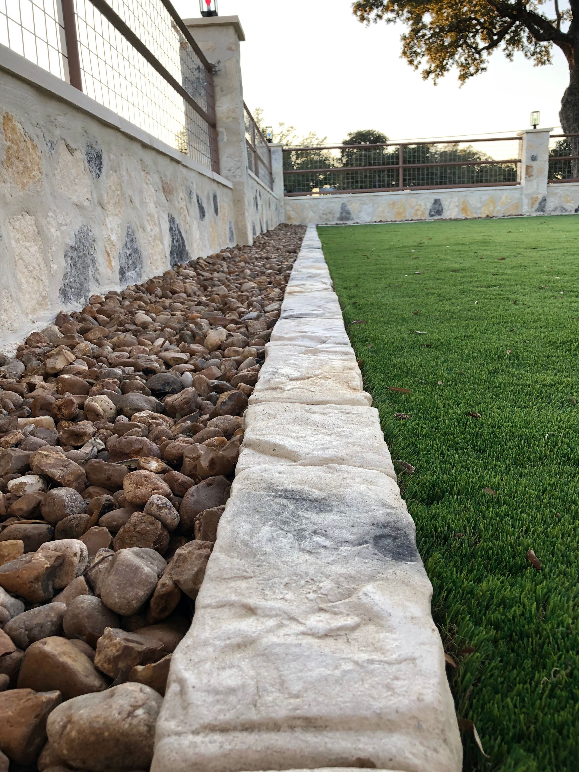 There is a stone border between the grass and the rocks.