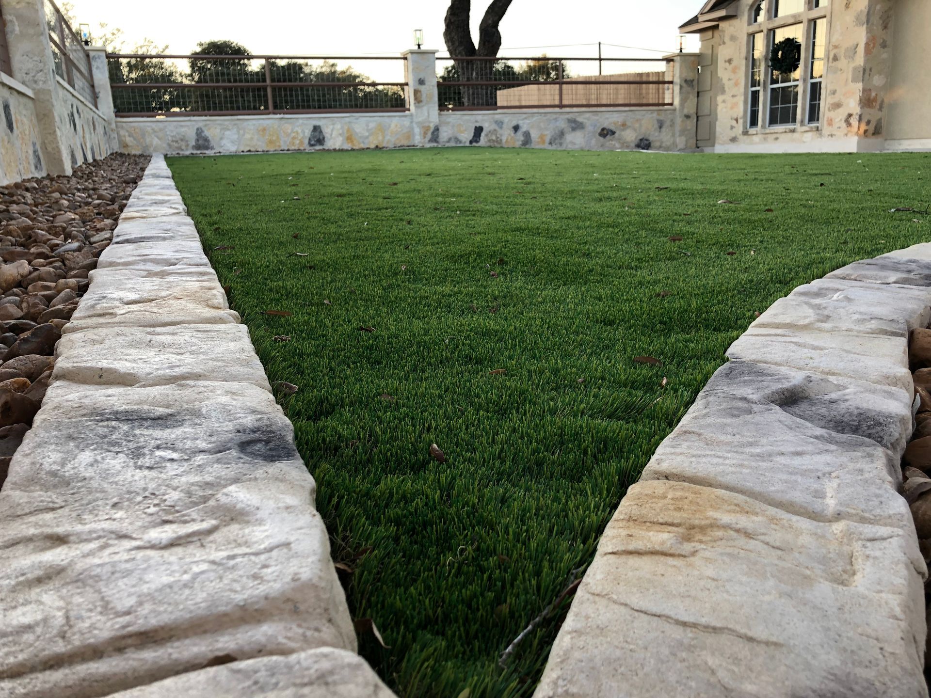 A lawn with a stone border and a stone walkway leading to a house.