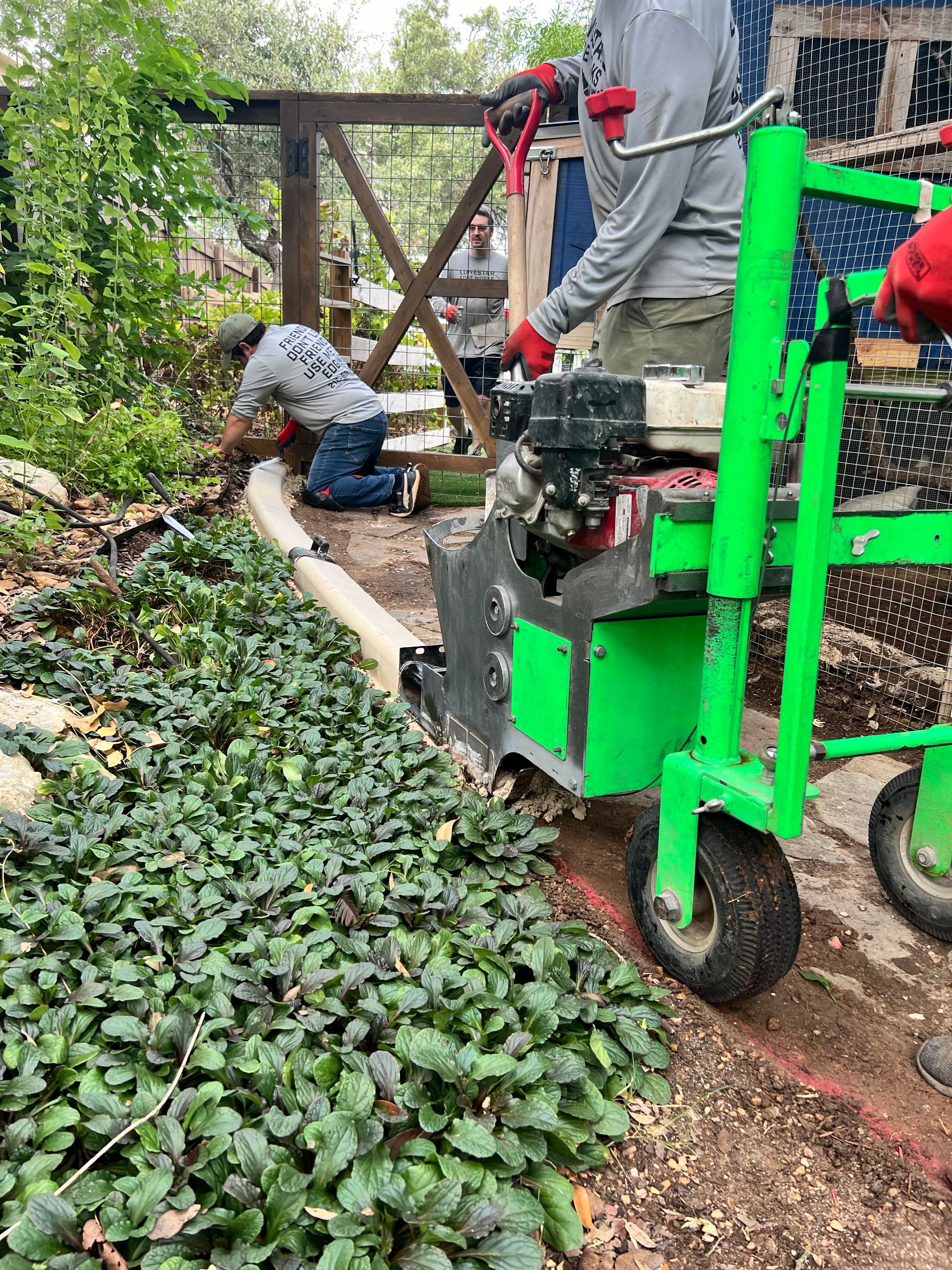 A man is kneeling down next to a green machine in a garden.