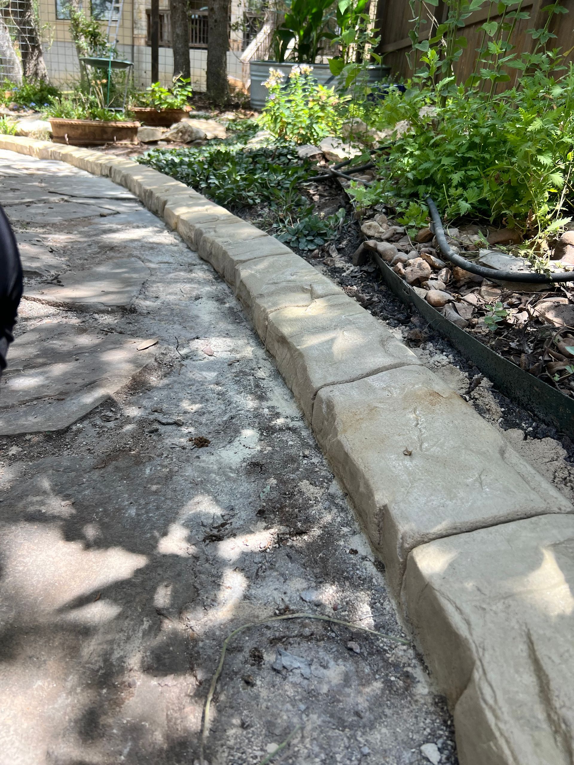A person is walking down a sidewalk next to a garden.