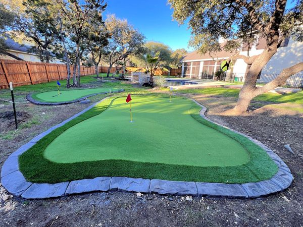 There is a putting green in the backyard of a house.
