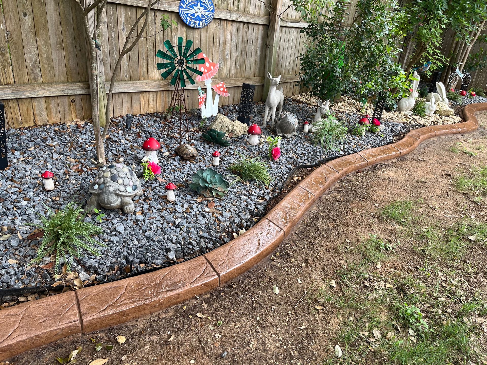 A concrete curb surrounds a gravel garden with gnomes and mushrooms.