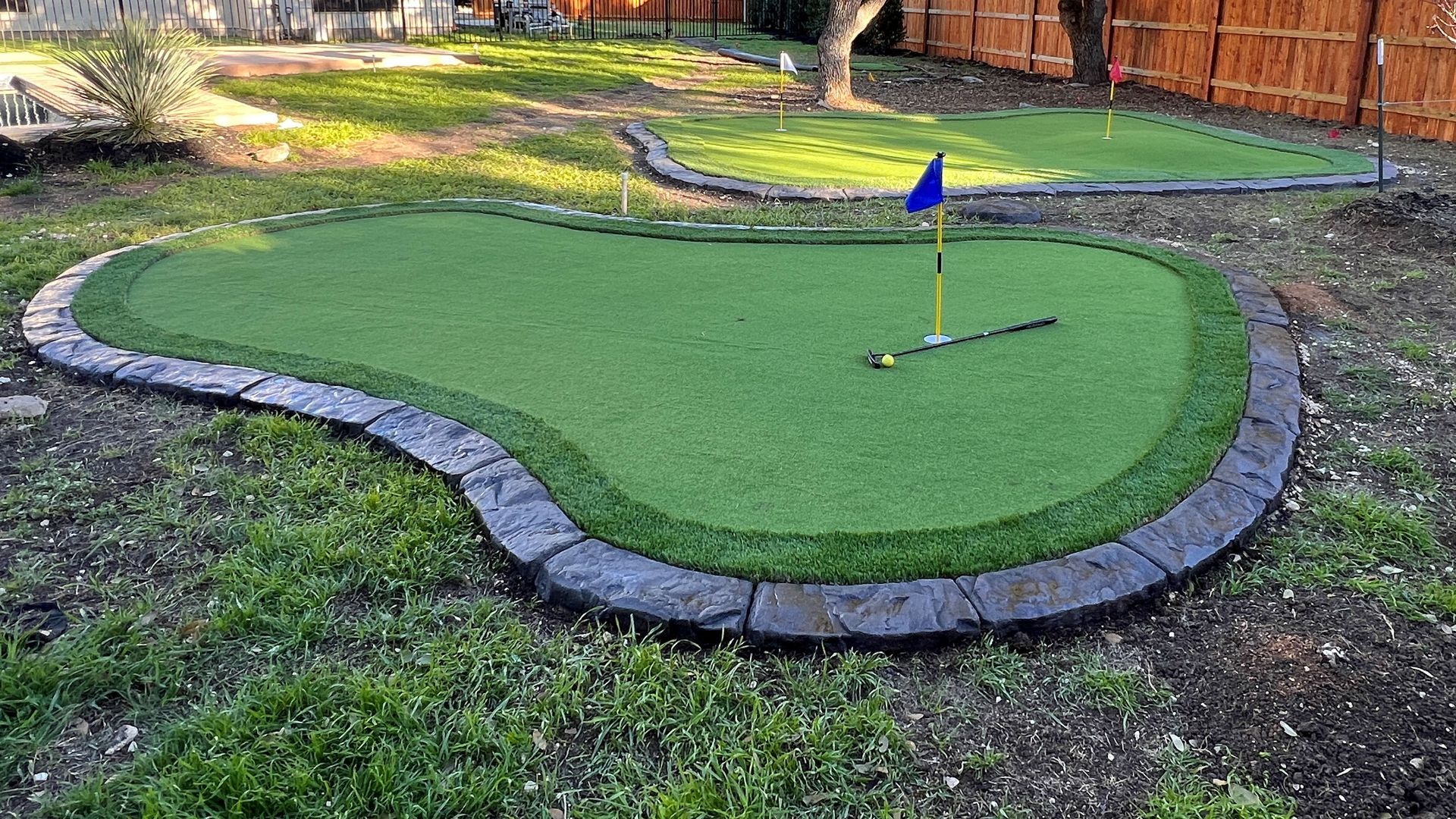 A small putting green in a backyard with a flag.