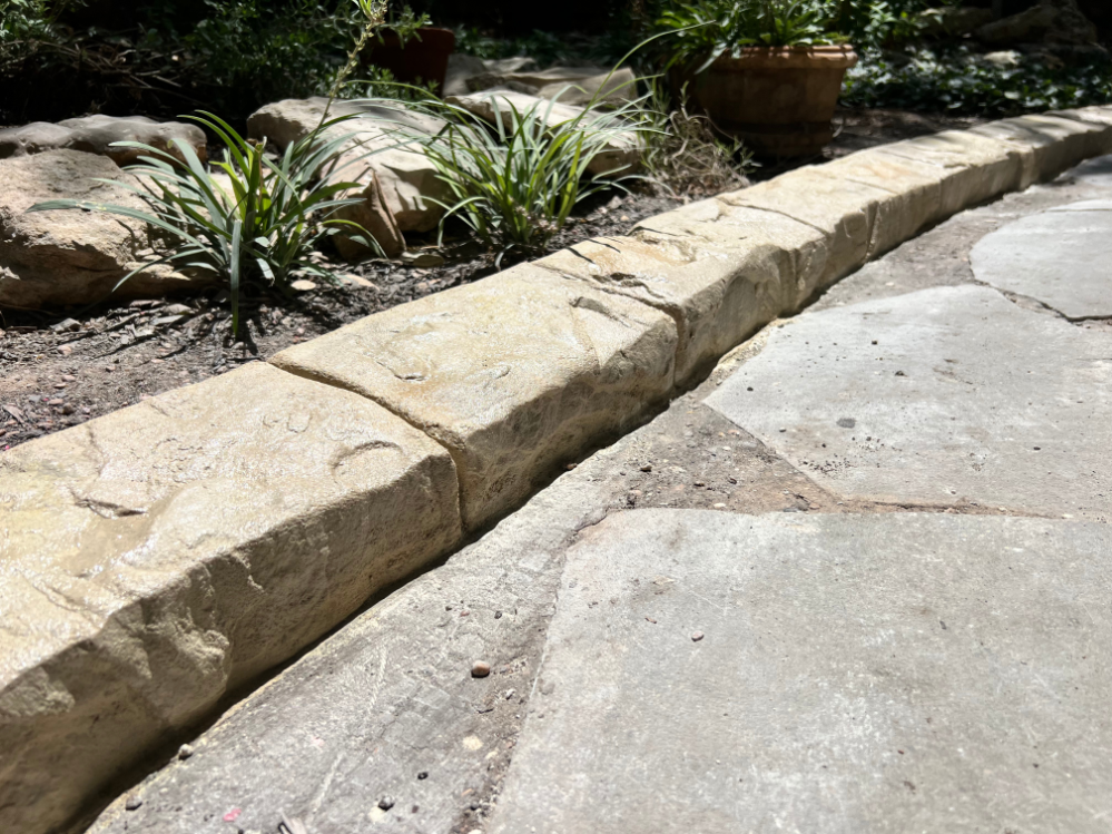 A stone curb is surrounded by plants and rocks in a garden.