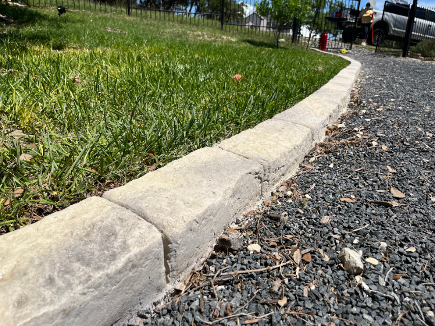 A concrete curb is surrounded by grass and gravel on the side of a road.