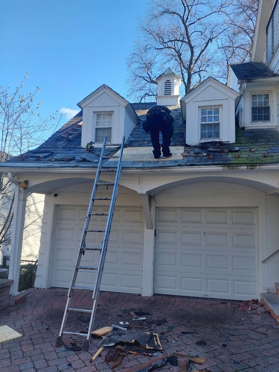 A man is standing on the roof of a house with a ladder.