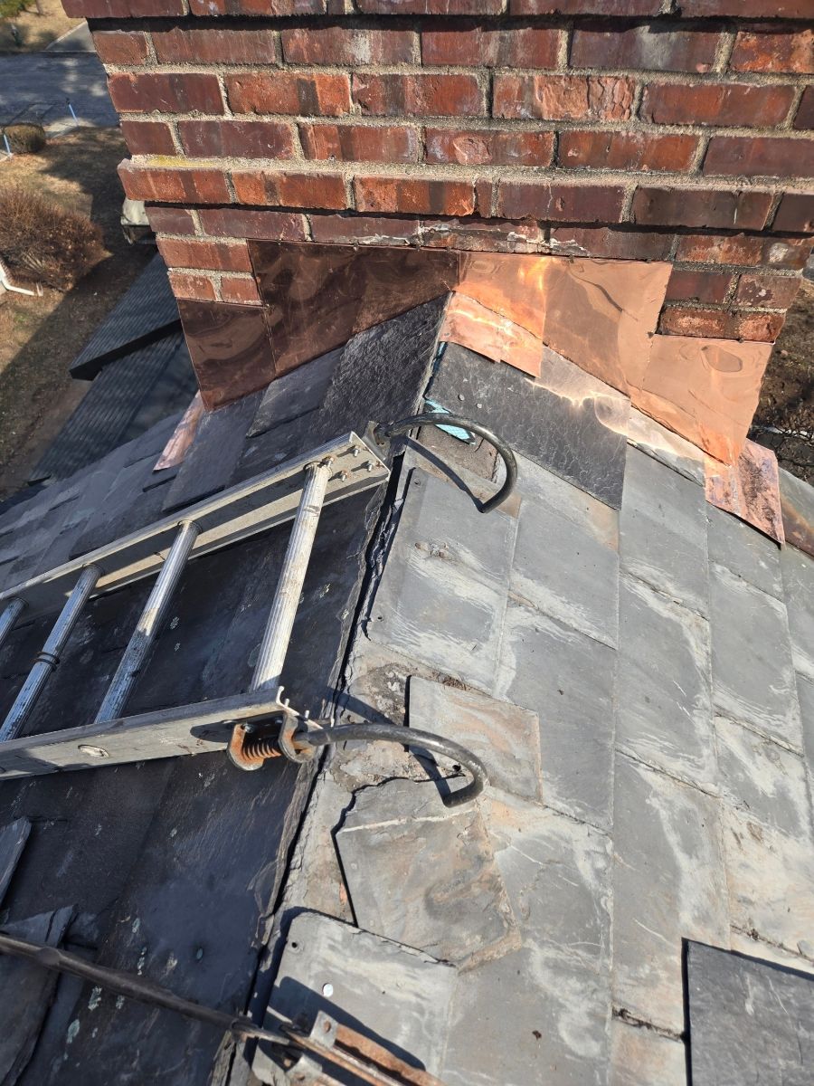 A ladder is sitting on top of a roof next to a brick chimney.