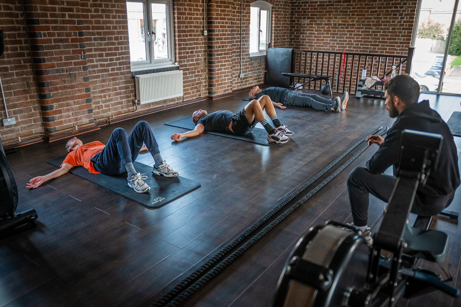 Red candle burning brightly on a black surface, three people in the background lying down in a workout room.