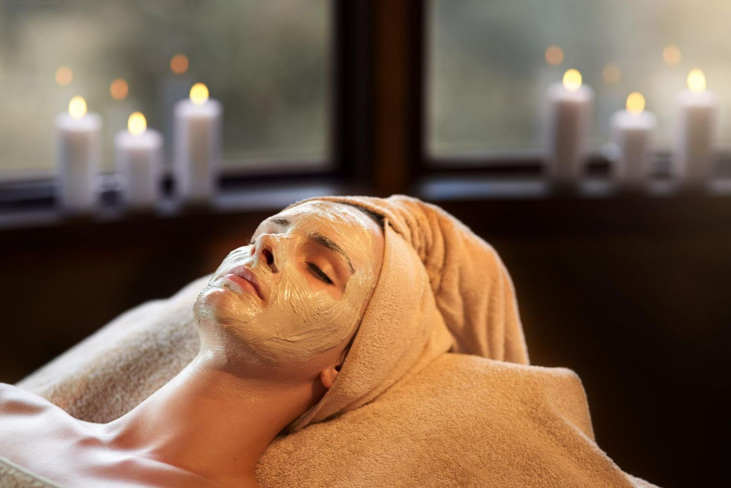 Person with facial mask relaxing at a spa, candles in background.