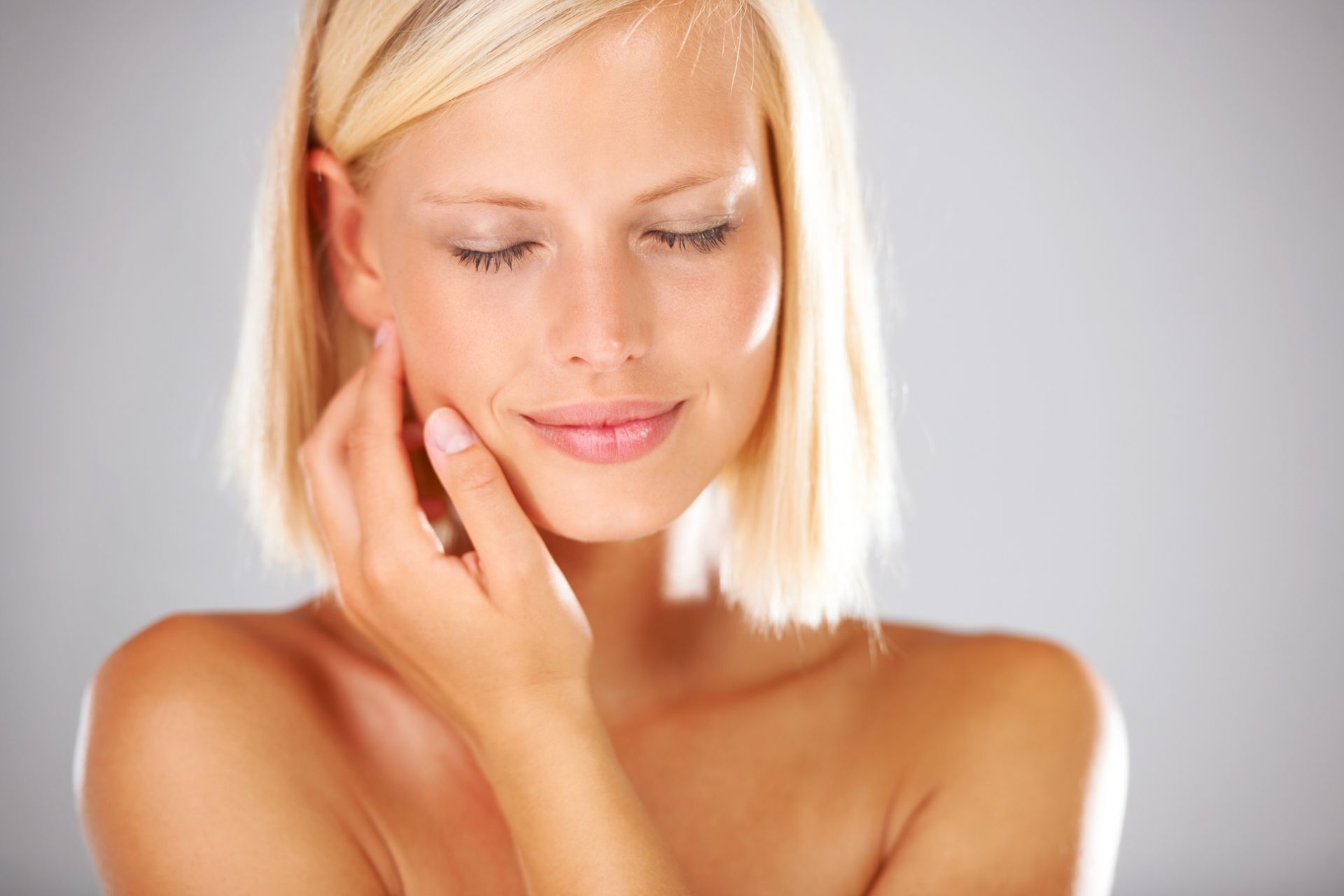 A woman is touching her face with her hand and smiling.