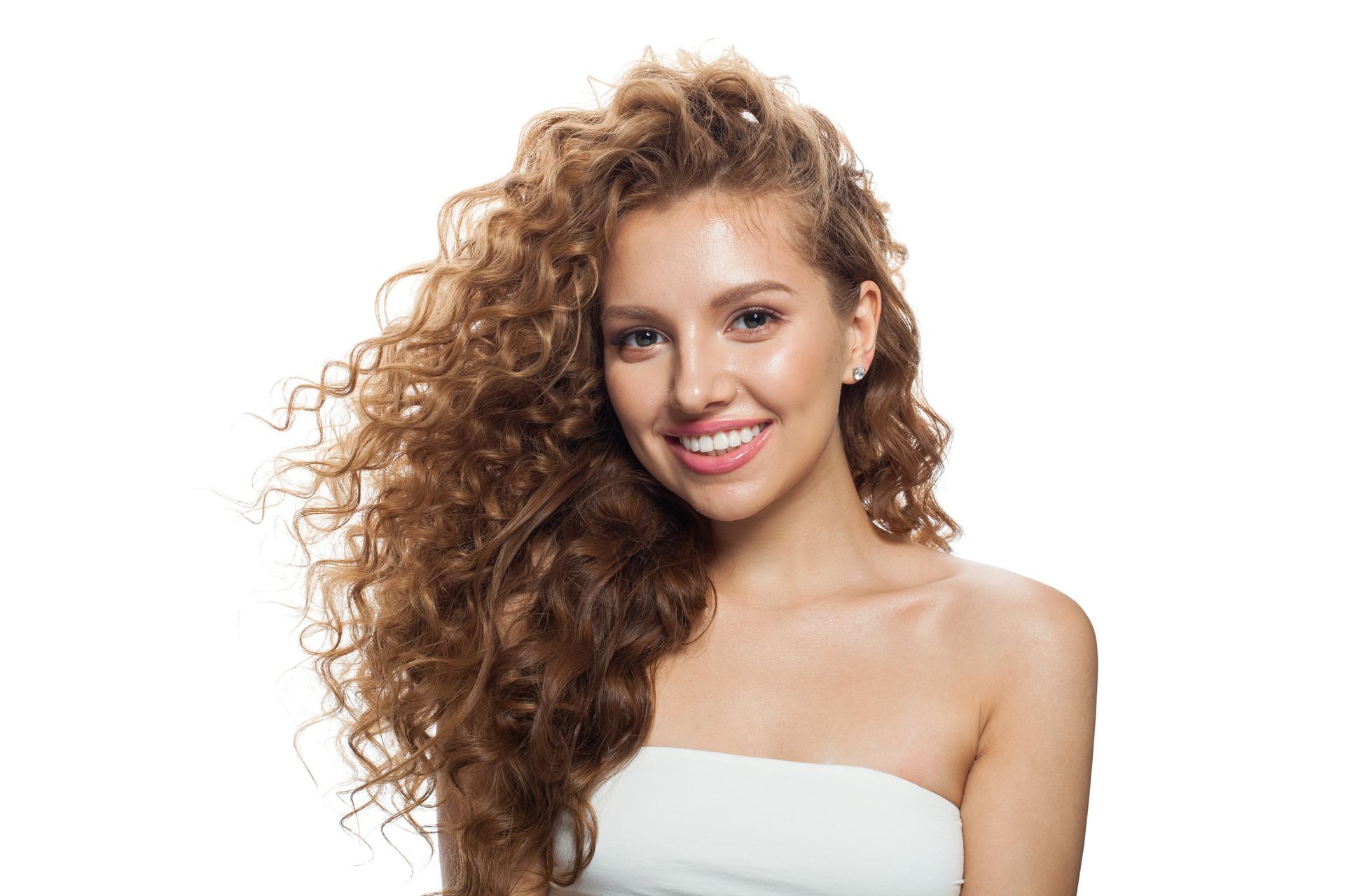 A woman with long curly hair is smiling and wearing a white strapless top.