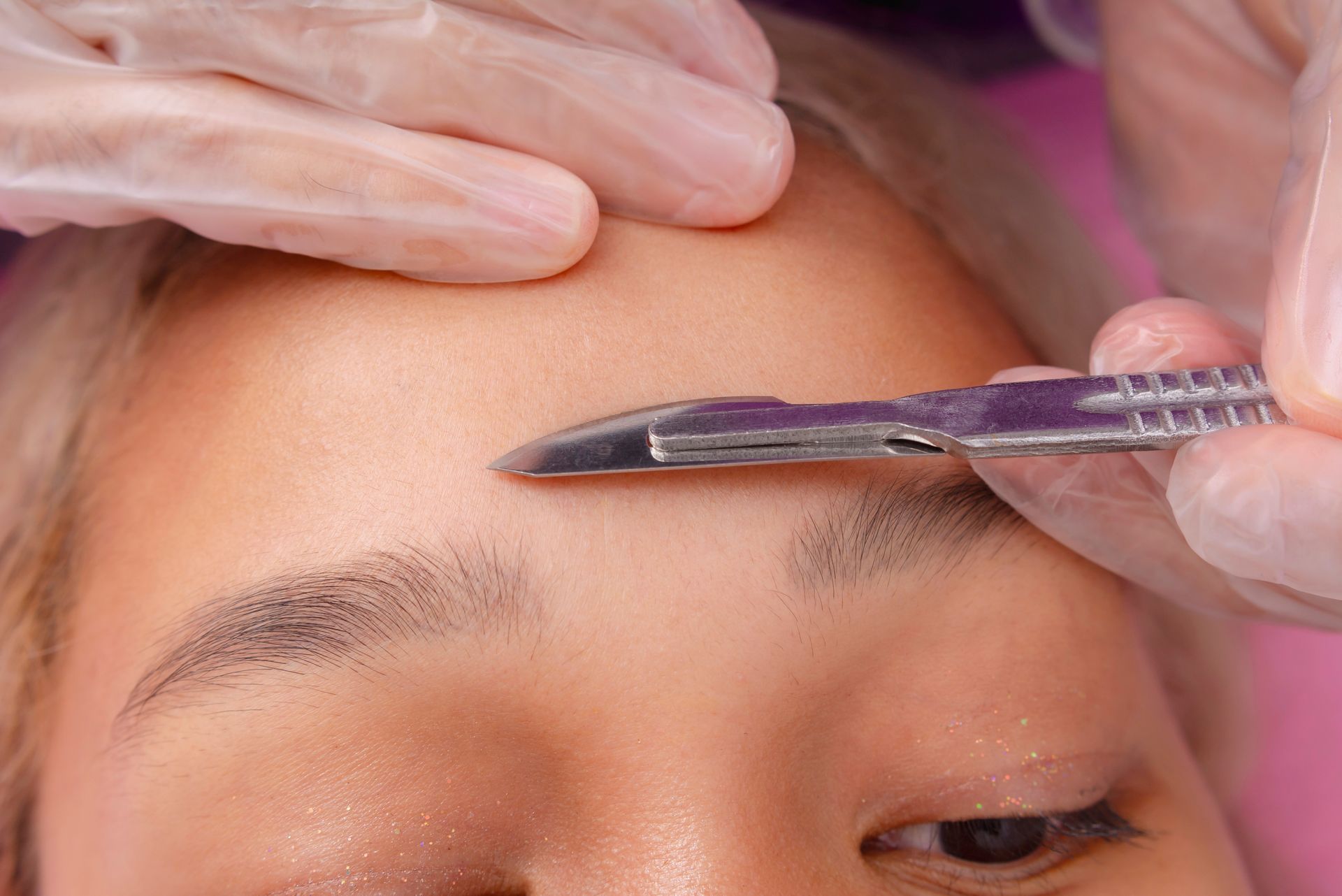 A woman is getting her eyebrows trimmed with a razor.
