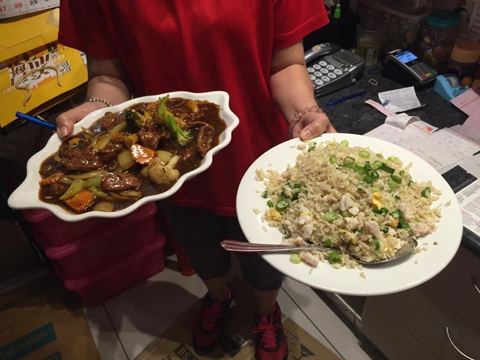 A Woman is Holding Two Plates of Food in Her Hands — Red Lantern Chinese Restaurant In Palmerston City, NT