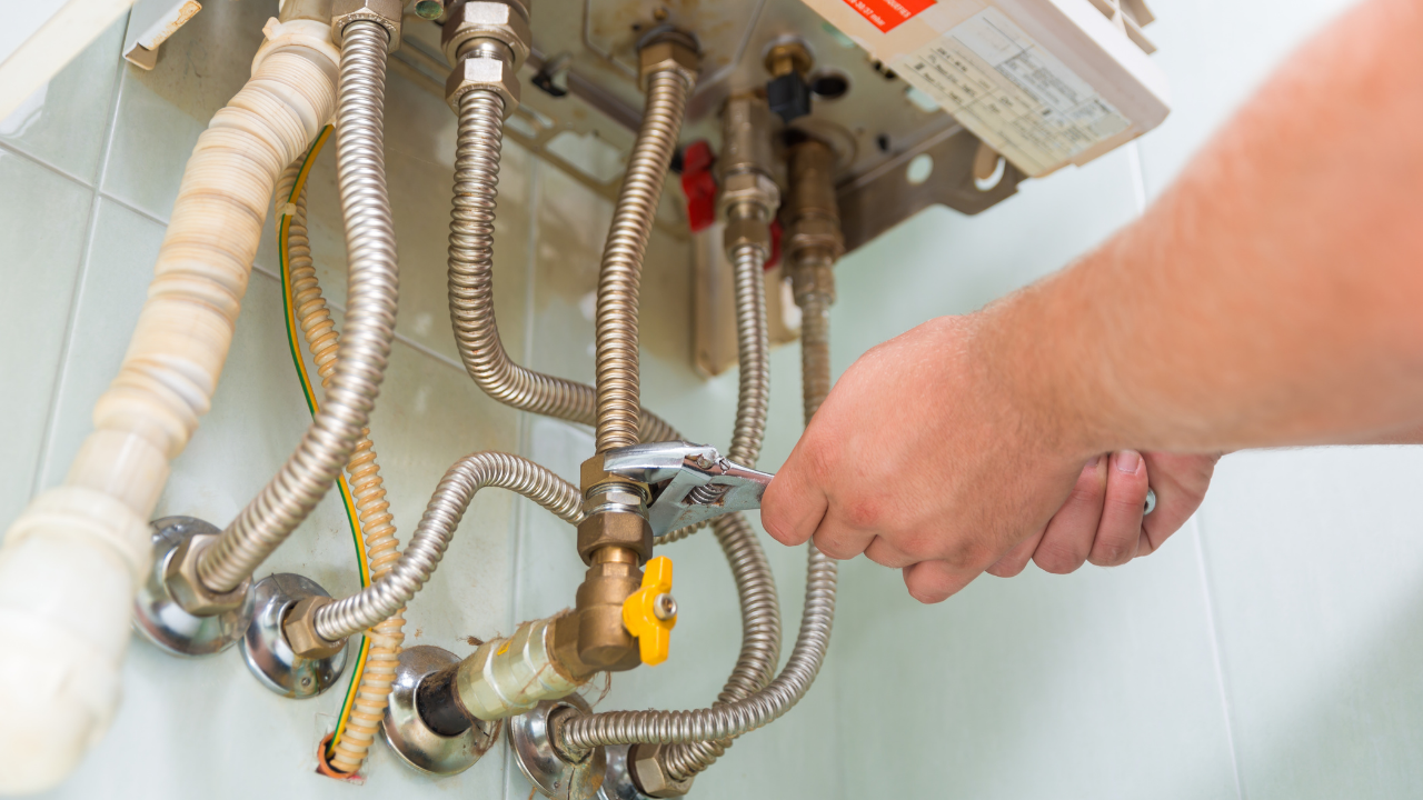 Person using a wrench to work on a water heater, with various pipes and valves.