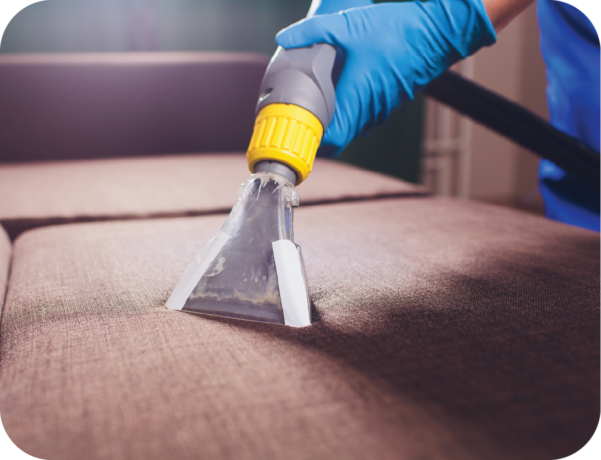 A person is cleaning a couch with a vacuum cleaner.