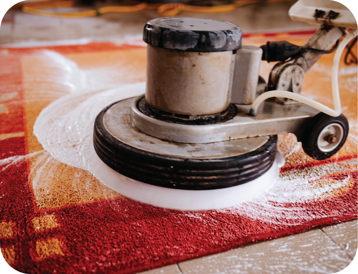 A machine is cleaning a red rug on the floor.