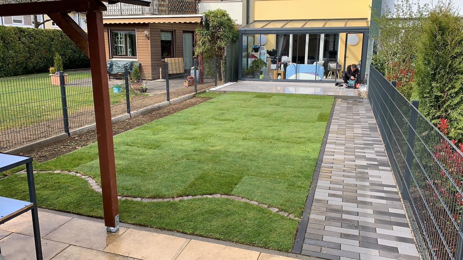 Ein üppiger grüner Rasen ist von einem Ziegelweg und einem Zaun umgeben.