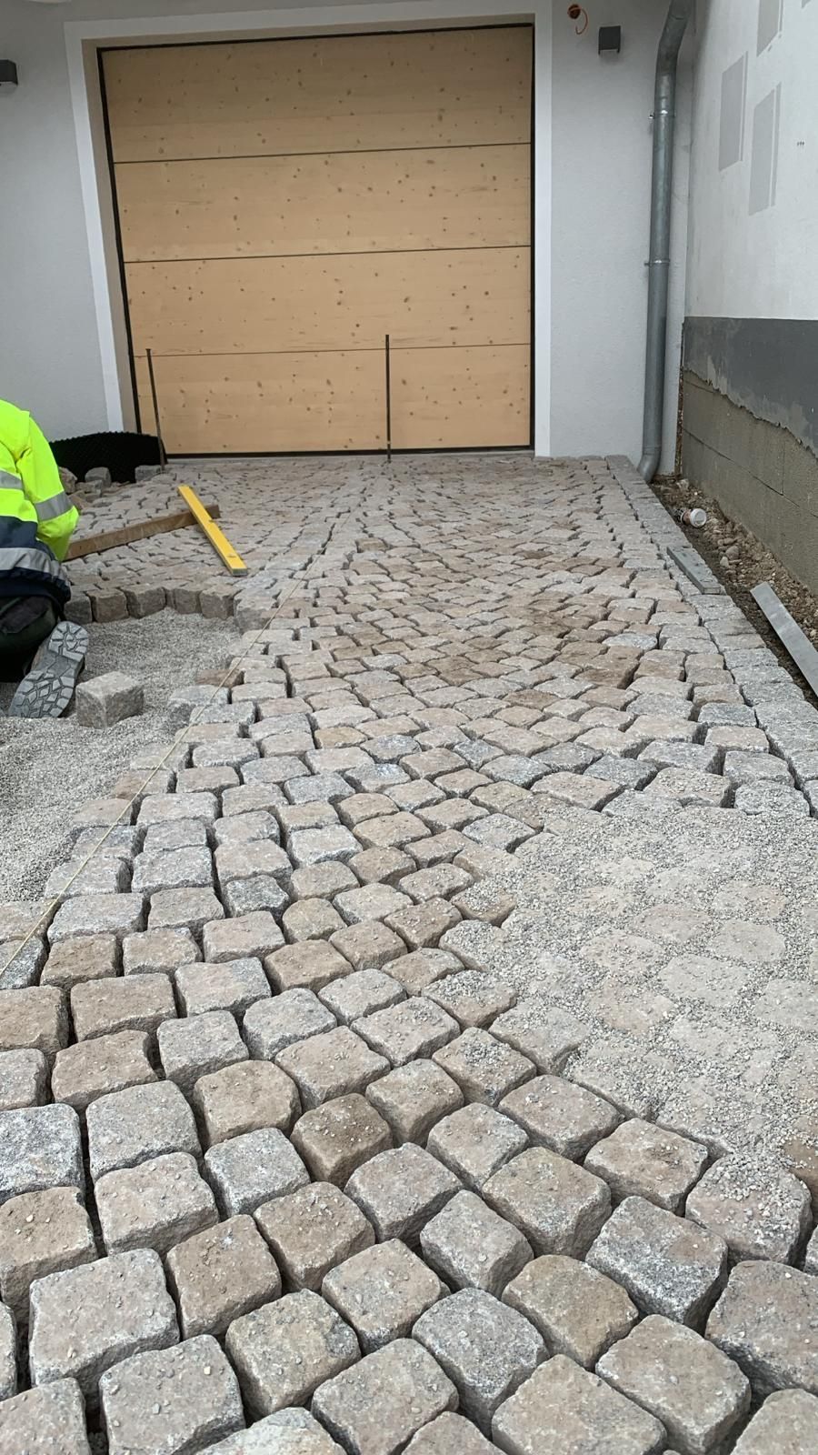 Ein Mann legt Ziegelsteine ​​in einer Einfahrt vor einem Garagentor.