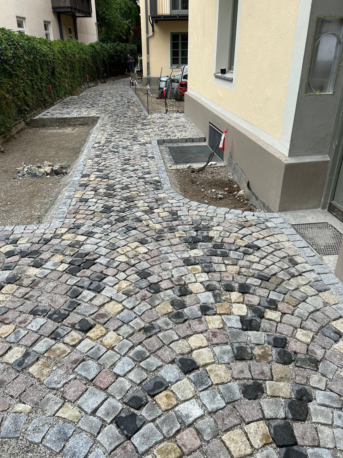 Vor einem Gebäude wird ein gepflasterter Gehweg gebaut.