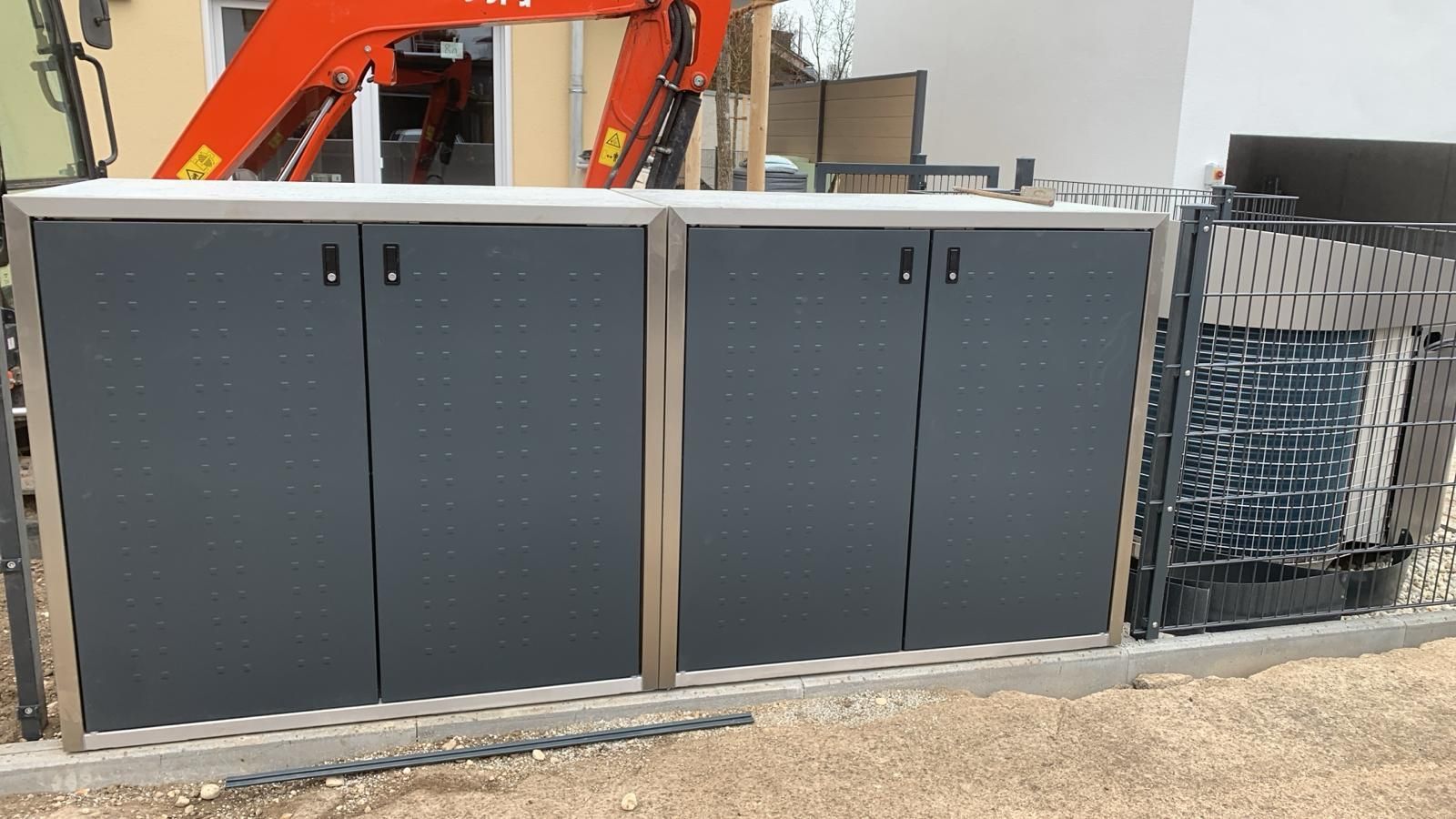 Neben einem roten Kran steht ein großer grauer Schrank.