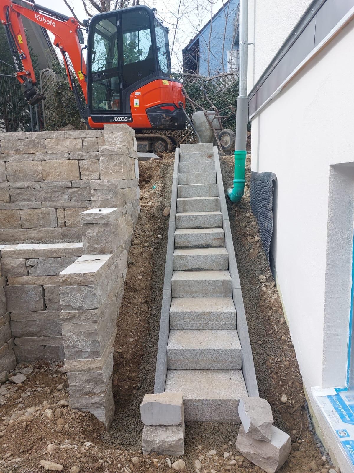 Neben einem Gebäude wird eine Treppe gebaut, im Hintergrund ein Bagger.