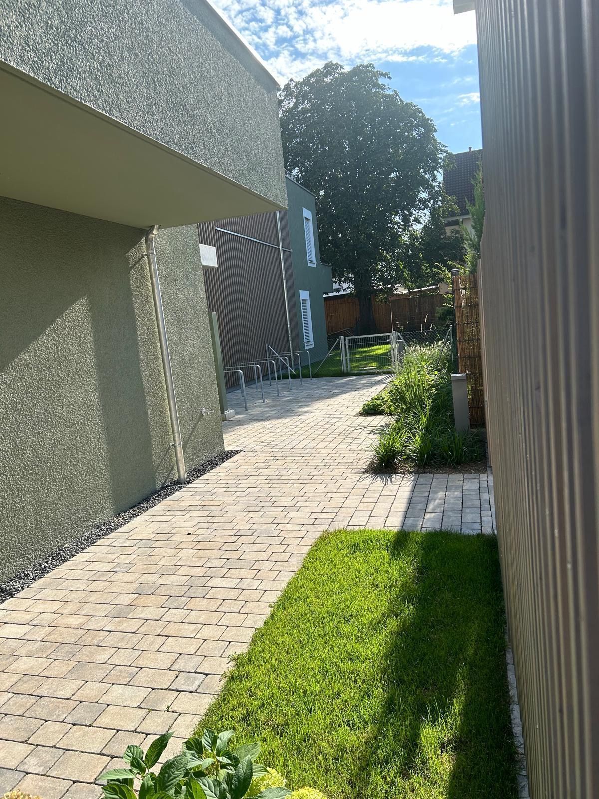 Ein gemauerter Gehweg zwischen zwei Gebäuden mit einem Zaun im Hintergrund.