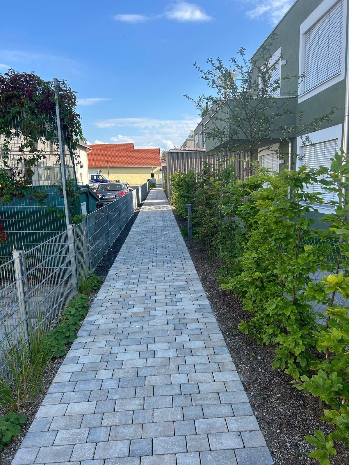 Ein gemauerter Gehweg führt zu einem Gebäude neben einem Zaun.