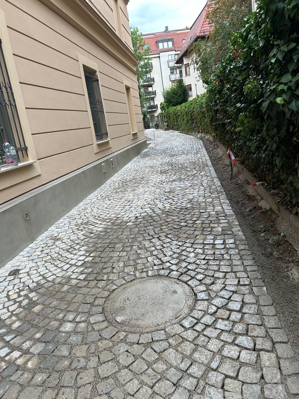 Eine gepflasterte Auffahrt, die zu einem Gebäude mit einem Gullydeckel in der Mitte führt.