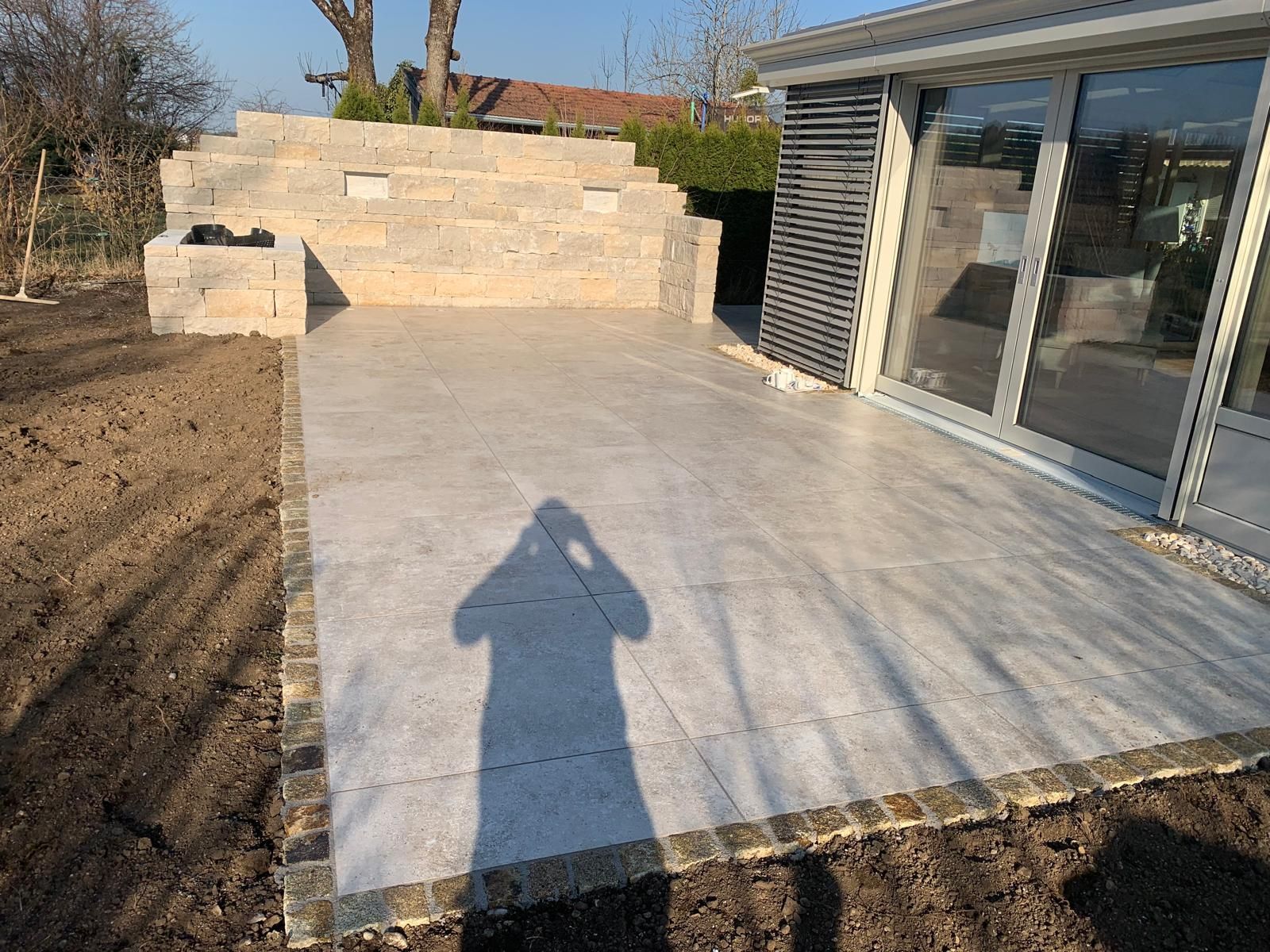 Der Schatten einer Person wird auf eine geflieste Terrasse vor einem Haus geworfen.