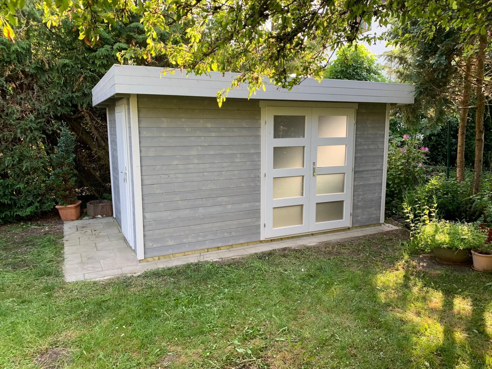 Inmitten eines üppig grünen Hofes steht ein kleiner weißer Schuppen.