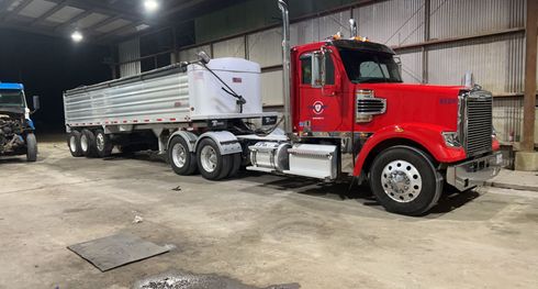 Red semi-truck with trailer parked inside a dimly lit industrial building.
