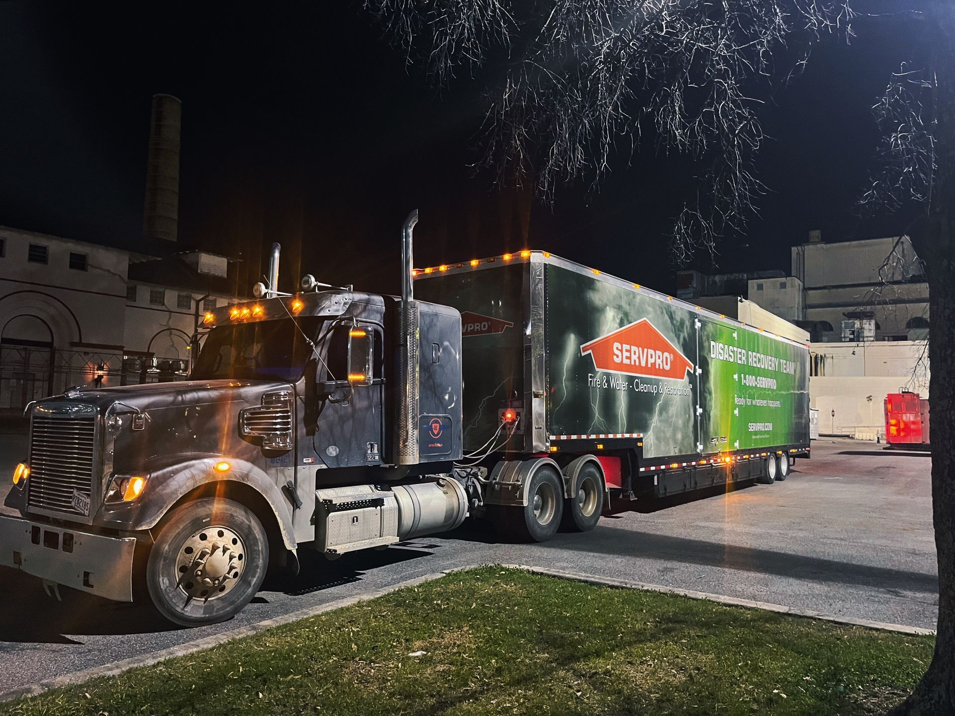 Dark, weathered semi-truck with a trailer, lit at night. The trailer has a green advertisement.