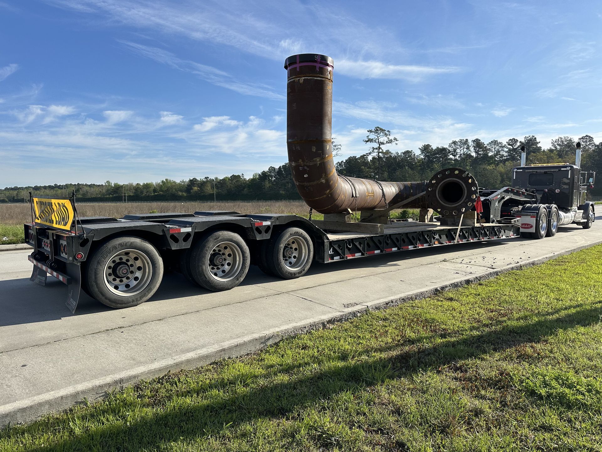 A large pipe section on a flatbed trailer, being transported by a semi-truck on a road.