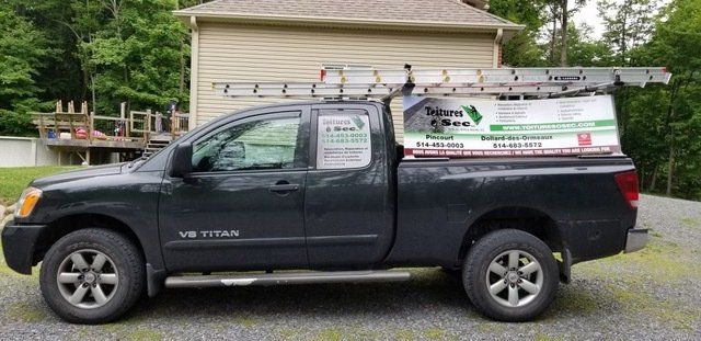 Un camion noir avec une échelle dessus est garé devant une maison.
