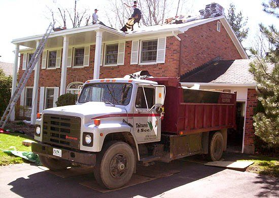 Un camion à benne basculante est garé devant une maison en briques