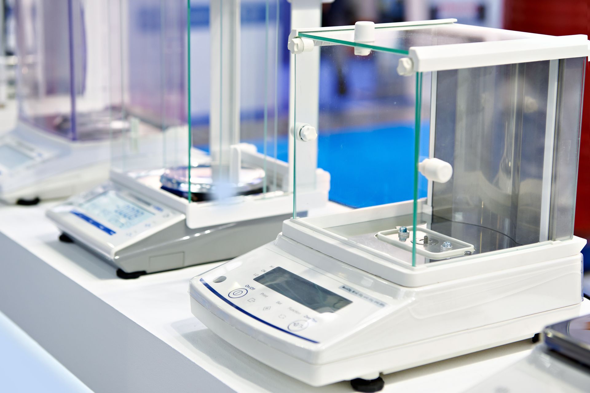 Several laboratory analytical balances with glass draft shields lined up on a white surface.