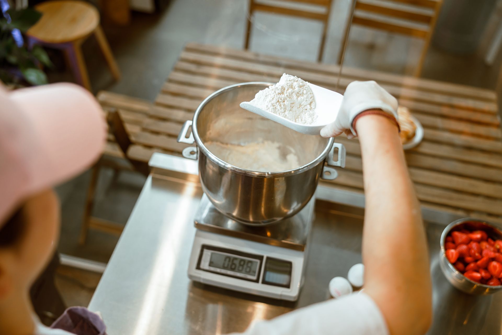 Baker pours white flour into a container to weigh on a digital scale.