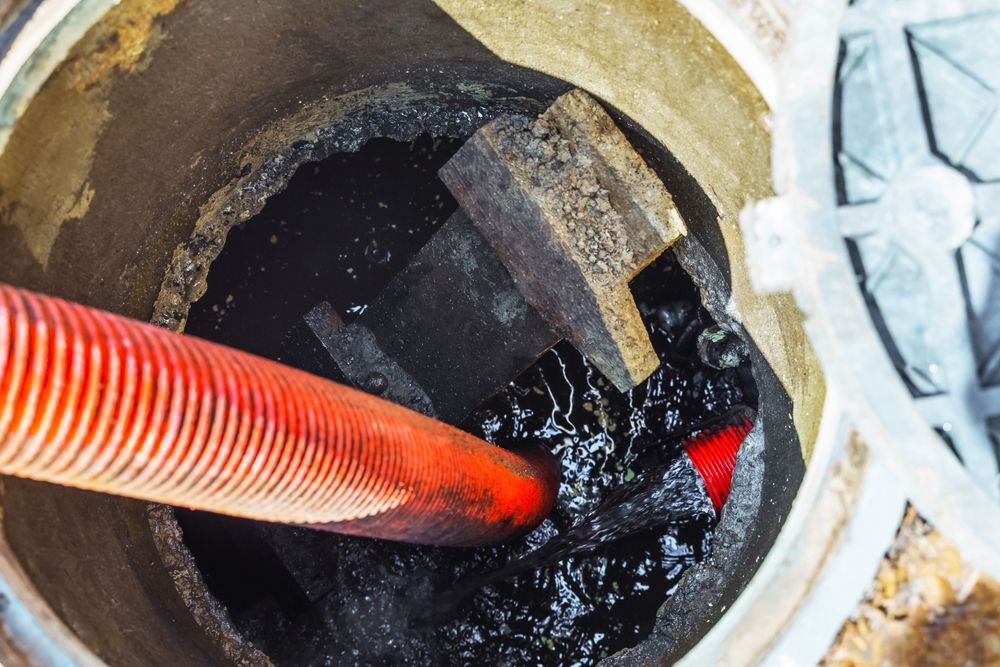 Inside a sewer access point, a red hose is inserted into thick, dark liquid.