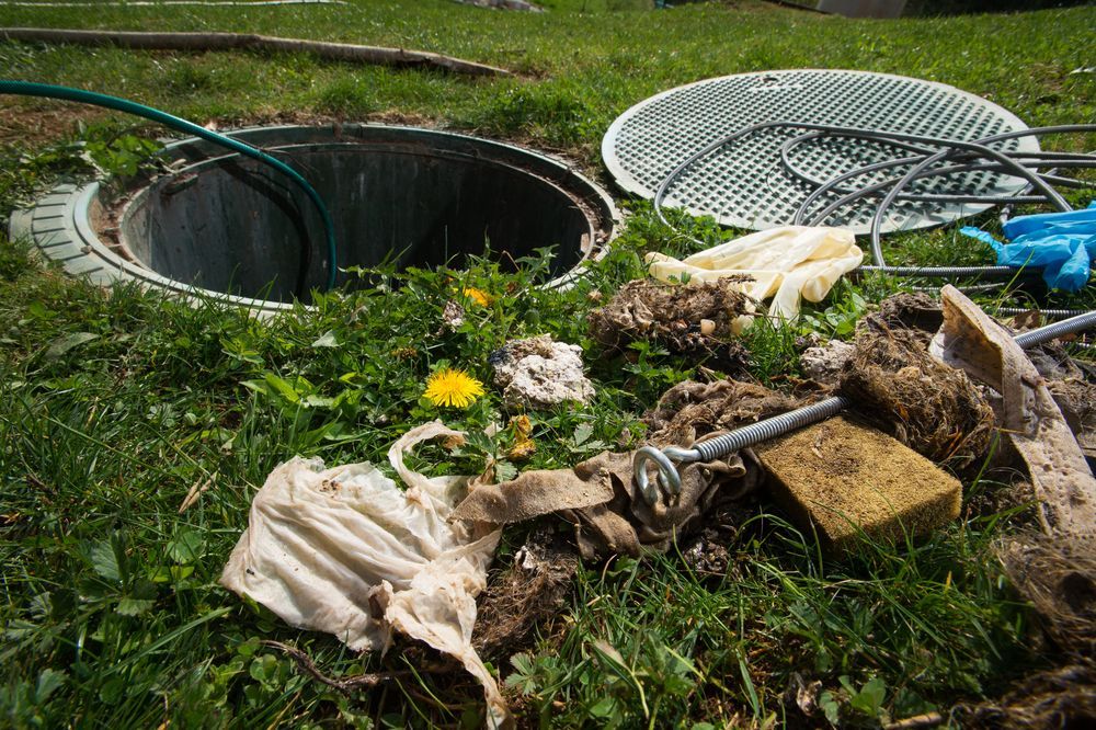 Open septic tank with debris and a hose on green grass.