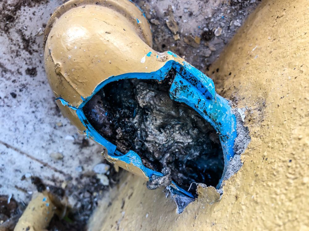 Broken, yellow pipe section, with a jagged tear exposing black interior and blue lining.