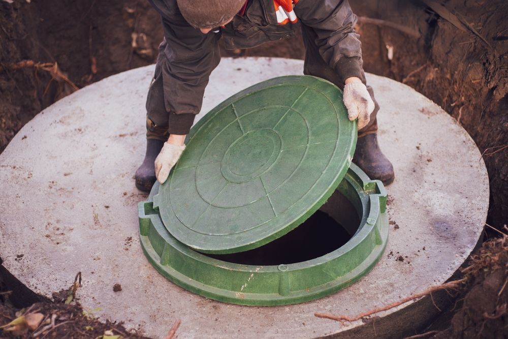 Person in dark work clothes placing a green lid on a concrete manhole.