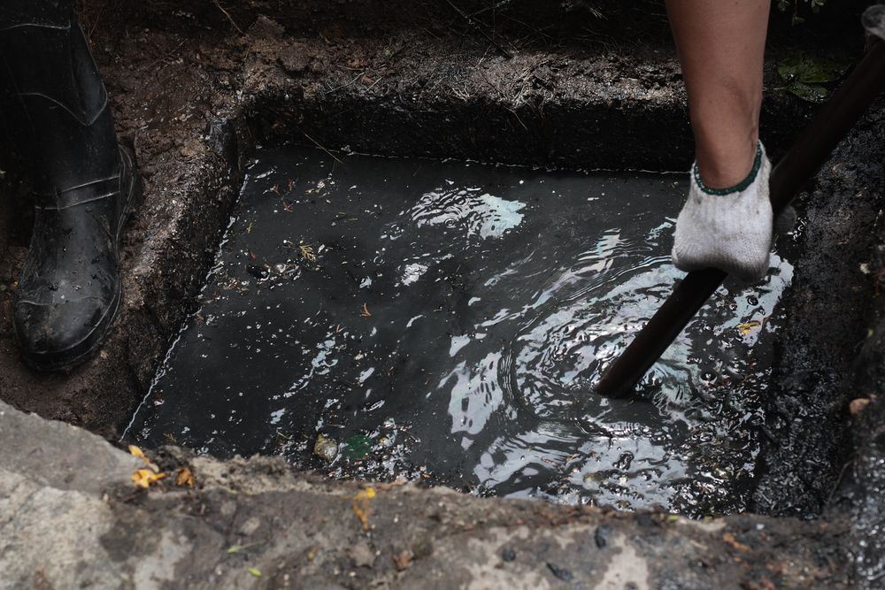 Person with glove stirring sewage in a rectangular opening.