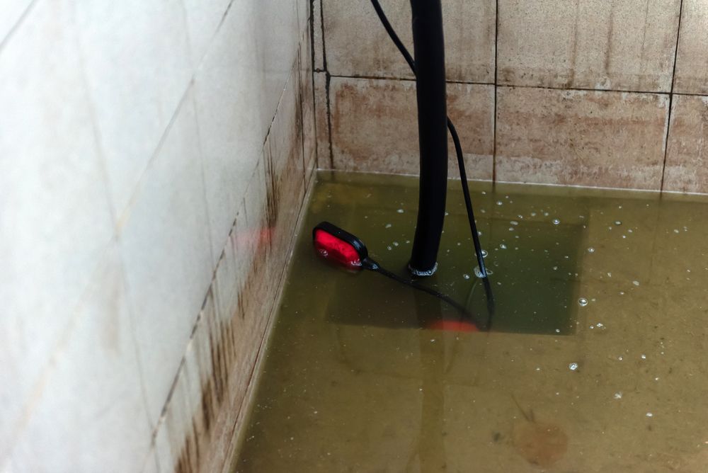 A flooded tiled utility room with a sump pump and float switch partially submerged in murky water.