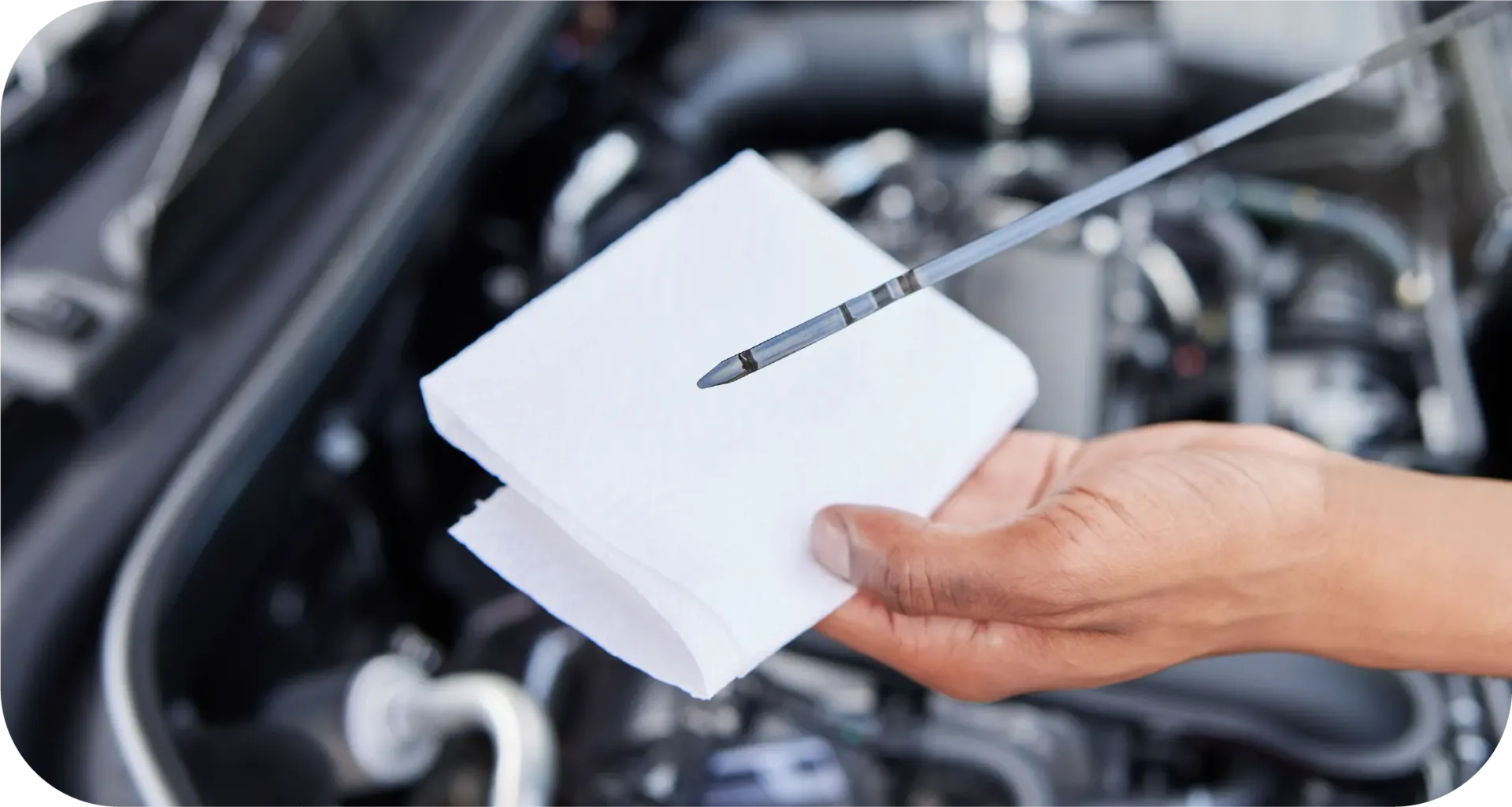 A person is holding a dipstick in front of a car engine.