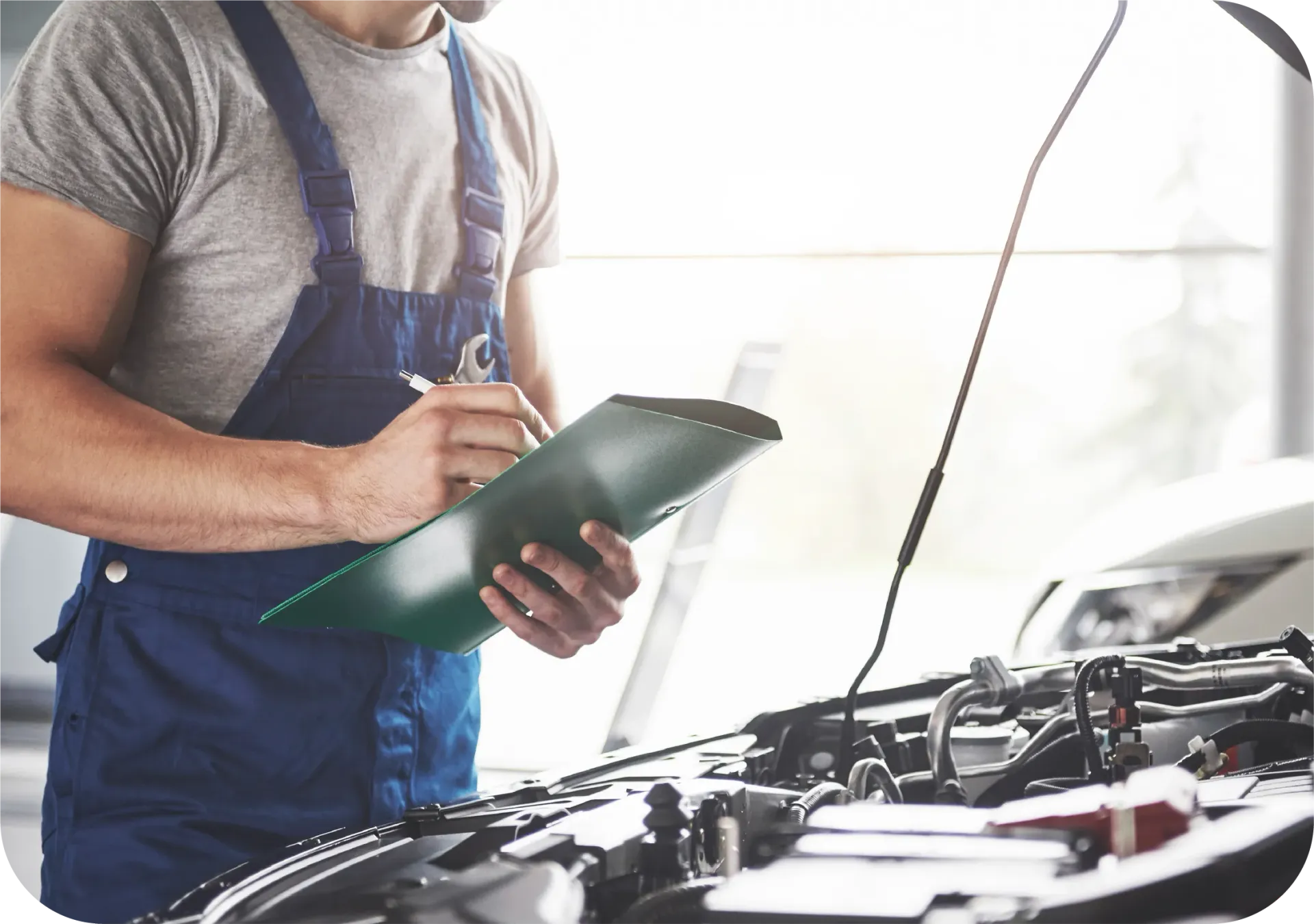 A man is looking under the hood of a car while holding a clipboard.